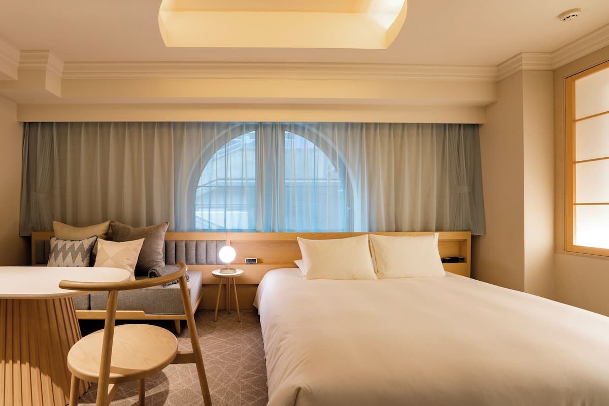 A hotel room with a bed, a desk, a chair, and a small table.