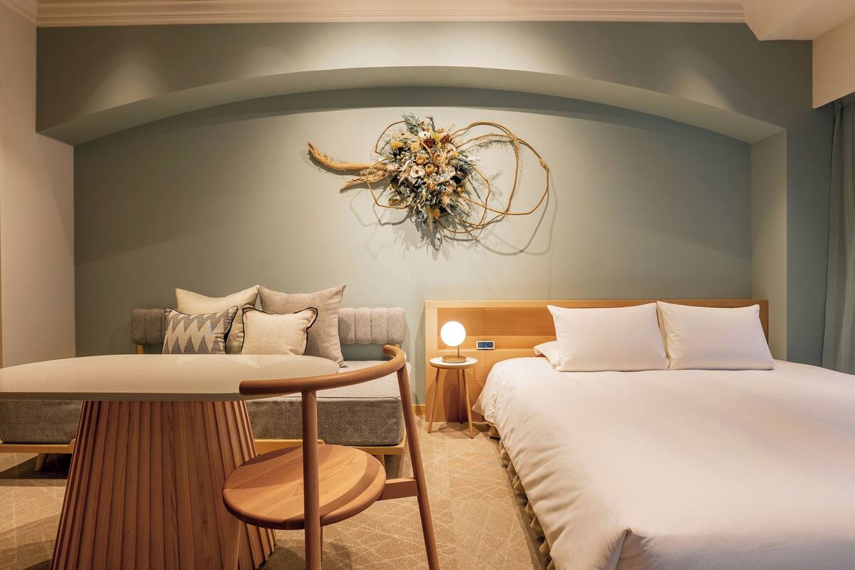 A hotel room with a bed, a sofa, a table, and a decorative wall piece.