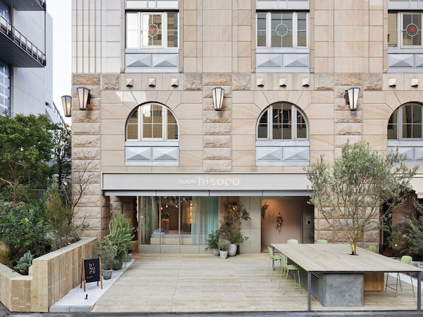 A hotel with a stone facade, large arched windows, and a welcoming entrance with a wooden bench and potted plants. - hotel hisoca ikebukuro (Tokyo)