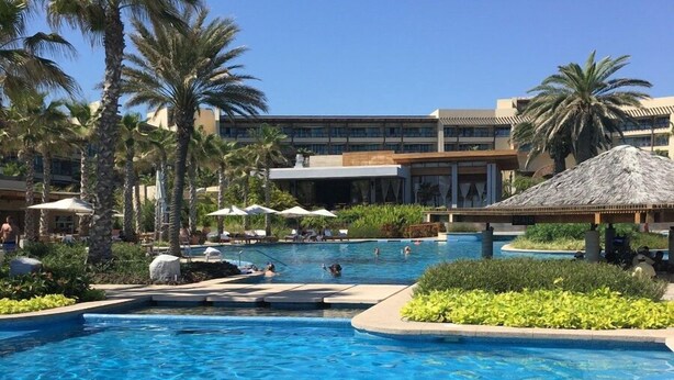 A swimming pool with clear blue water, surrounded by palm trees and a building with a thatched roof. - Chic 1-bedroom apartment with WiFi, AC in beautiful San Jose del Cabo (San Jose del Cabo)