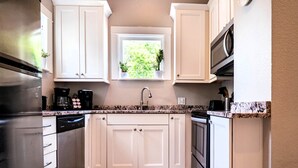 A kitchen with white cabinets, a stainless steel refrigerator, a coffee maker, and a window with a view of greenery.