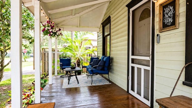 A covered porch with two blue chairs and a small table, wooden flooring, and a door with a 'Home Sweet Home' sign.