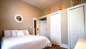 A bedroom with a bed, wooden flooring, white walls, and a white wardrobe.