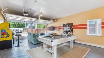 A pool table in a room with a yellow wall, a mounted TV, and a window with blinds.