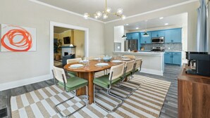 Una cocina moderna con armarios azules, una isla central y una zona de comedor con mesa de madera y sillas verdes.