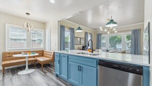 Una cocina moderna con lavavajillas integrado, armarios azules y una zona de comedor con banco y mesa.