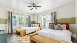 Un dormitorio con dos camas, ventilador de techo y ventanas amplias con cortinas.