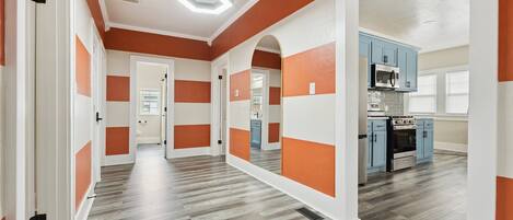 A spacious hallway with a modern kitchen area featuring blue cabinets and stainless steel appliances.