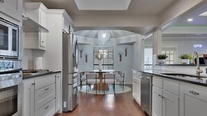 A modern kitchen with stainless steel appliances, a central island with chairs, and a chandelier. - Mini Golf | Pool | Game room | Stylish & Spacious | Wifi | Free Parking (Dallas)