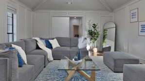 A modern living room with a grey sectional sofa, a glass coffee table, and a blue patterned rug. - Mini Golf | Pool | Game room | Stylish & Spacious | Wifi | Free Parking (Dallas)