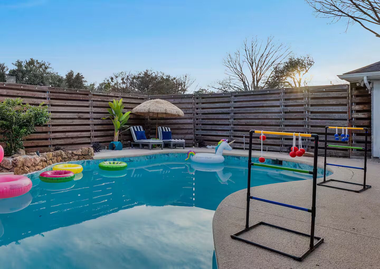 Un jardin avec une piscine, des bouées gonflables, une petite licorne gonflable et un jeu de corde à sauter.