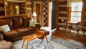 A rustic cabin interior with a leather sofa, wooden dining table, and patterned rug.
