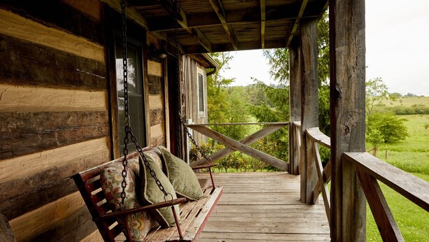 A wooden porch with a swing, a wooden railing, and a view of a green landscape.
