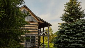 A log cabin with a wooden porch and a large evergreen tree in the foreground.