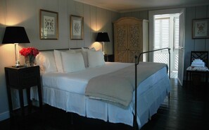 A neatly made bed with white linens, two bedside lamps, a vase with red flowers, and a wooden wardrobe. - Ultimate Island Style House w/Pool in Large Walled Garden in Historic Dunmore Town (Dunmore Town)