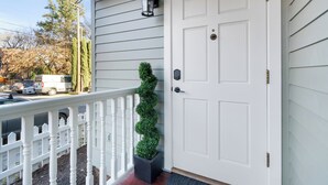 Une porte blanche avec une boîte aux lettres noire, une clôture en bois peinte en blanc et un pot de fleurs placé à côté de la porte.