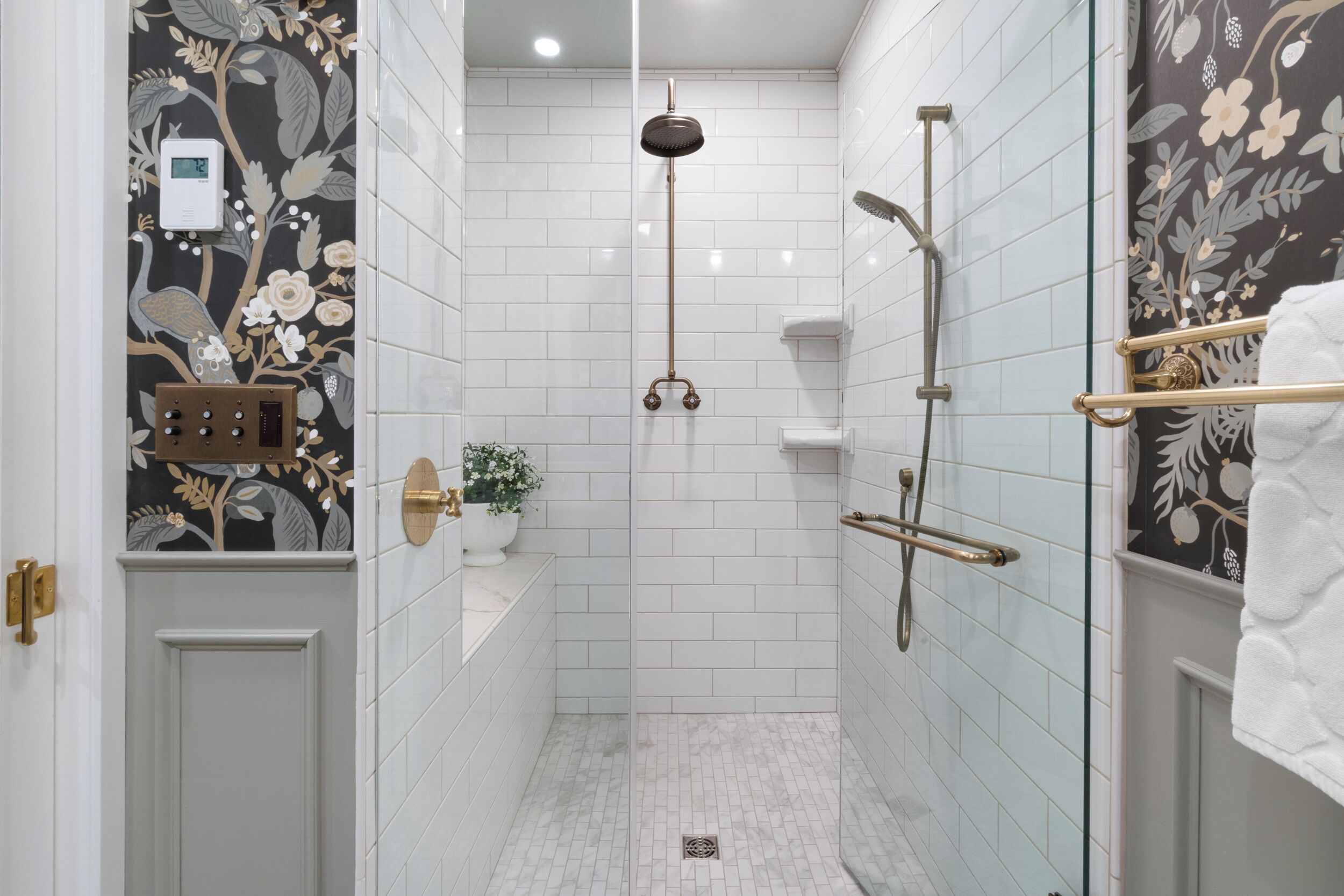 Un baño moderno con azulejos blancos, una ducha con cabezal de mano, un inodoro y una pared decorativa con motivos florales.