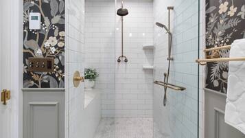 Un baño moderno con azulejos blancos, una ducha con cabezal de mano, un inodoro y una pared decorativa con motivos florales.