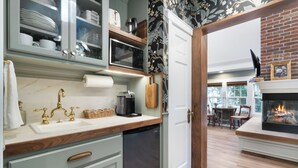 Une cuisine moderne équipée d’un lave-vaisselle, d’un four à micro-ondes et d’un plan de travail en bois. Un coin repas est aménagé, avec une cheminée en arrière-plan.
