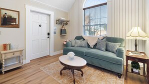 Un salon avec un canapé vert, une porte blanche, une petite table sur laquelle se trouve un vase, et une lampe sur une table d’appoint.