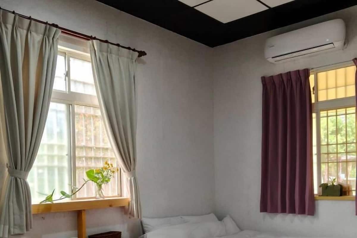 A hotel room with two beds, a desk, and an air conditioning unit.