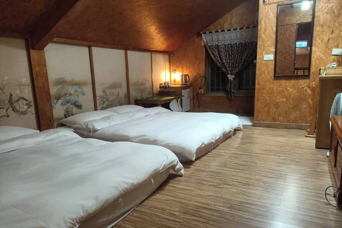 A room with two beds, a small table with a lamp, and a window with curtains.