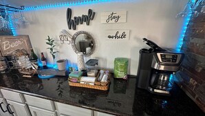 Un comptoir de cuisine avec une machine à café, un grille-pain et un miroir. On y trouve également divers ustensiles de cuisine et un panneau indiquant « Location de courte durée ».