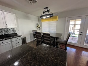 A kitchen with granite countertops, white cabinets, a dining table with chairs, a yellow window valance, and a door leading outside. - 4-bedroom house in welcoming Goodyear,AZ with WiFi, AC. Enjoy your stay (Goodyear)