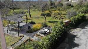 A view of a garden with a pergola, a small table, and chairs, surrounded by trees and a distant view of mountains and a body of water. - In the countryside, a cozy retreat for peaceful moments near Mount Vesuvius. (Torre del Greco)