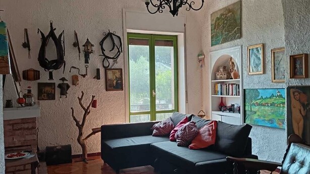 A cozy living room with a curved ceiling, a sectional sofa, a wooden chair, a fireplace, and various wall decorations. - In the countryside, a cozy retreat for peaceful moments near Mount Vesuvius. (Torre del Greco)