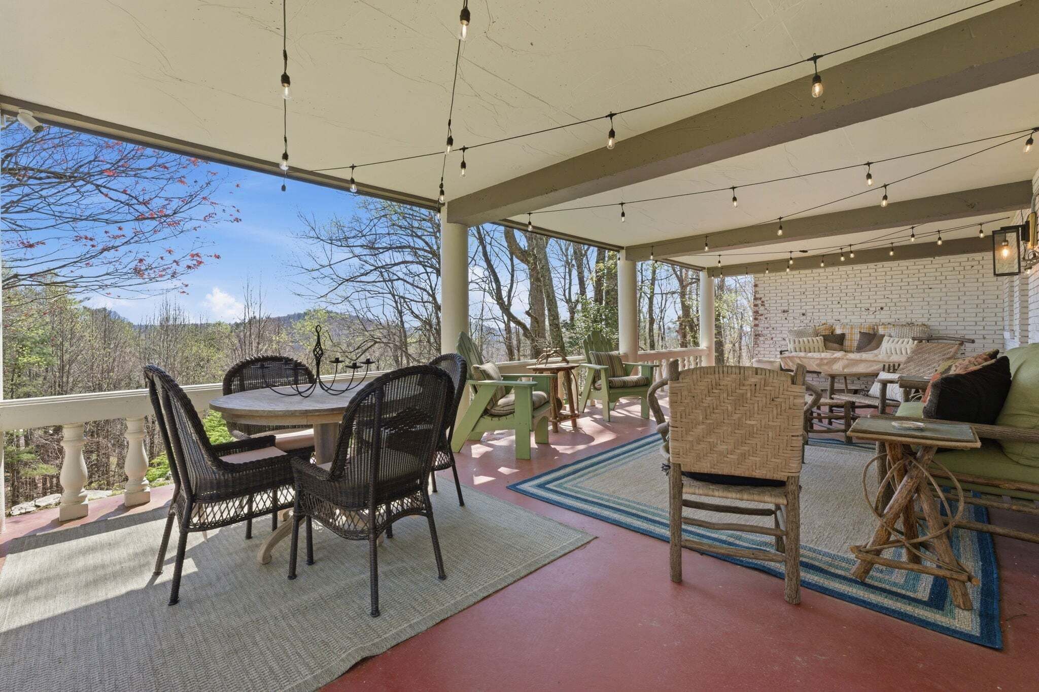 Eine überdachte Terrasse mit rundem Tisch und Stühlen, einem Sofa und einer Ziegelwand.