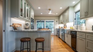 A modern kitchen with a central island, bar stools, and a view through the window. - The Bodhi: Spacious 5-bedroom retreat in Highlands with wooded mountain views. (Highlands)