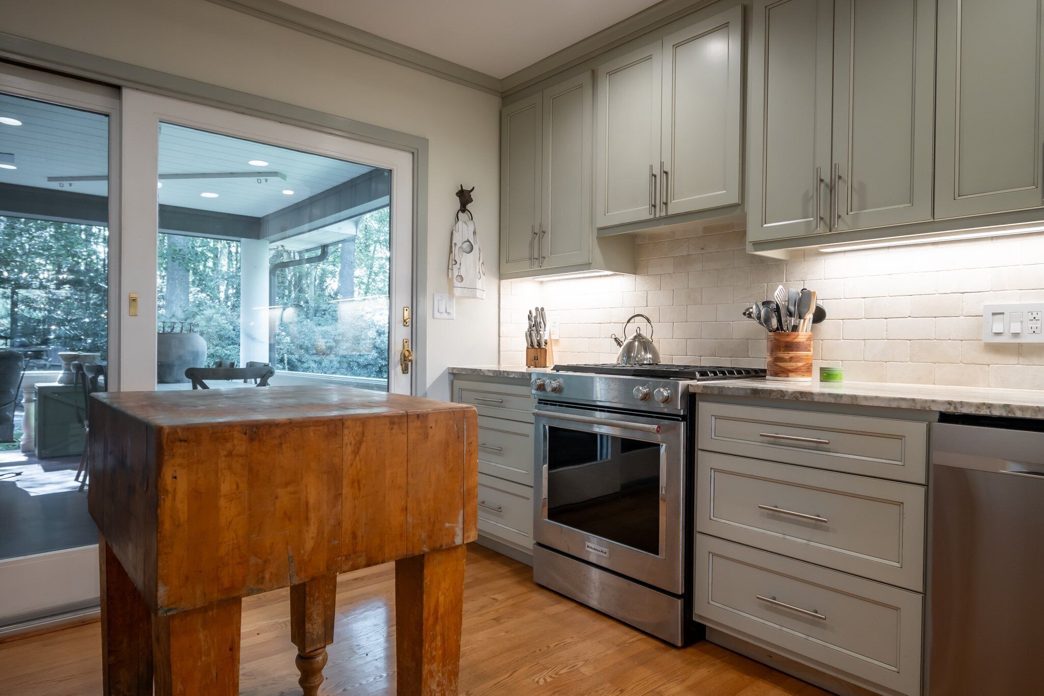 A modern kitchen with stainless steel appliances, grey cabinets, and a wooden table.