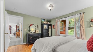 A bedroom with a large bed, a dresser, a mirror, and a window with curtains.