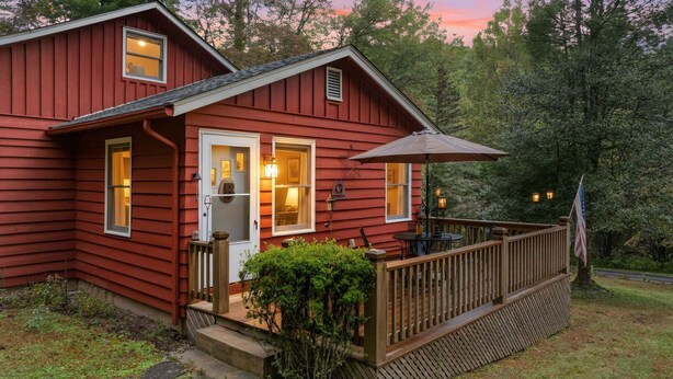 A red cabin with a porch, a deck, and a small table with an umbrella.