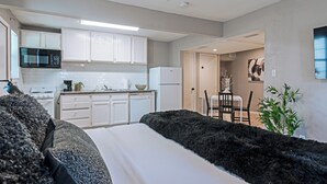 Una cocina moderna con armarios blancos, un microondas y un refrigerador. Hay un comedor con una mesa y sillas.