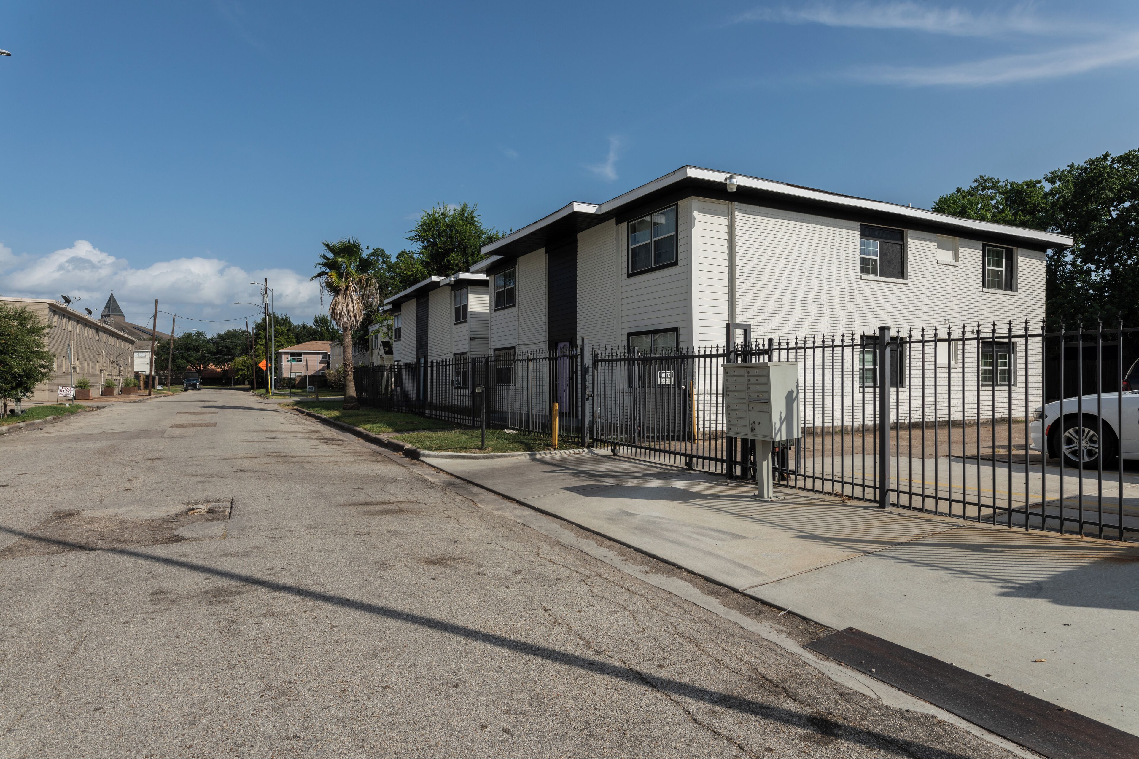 A residential street with a row of single-story houses, a sidewalk, and a parked car.