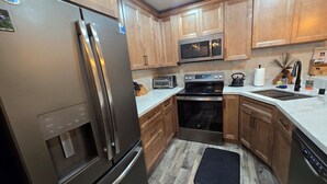 Una cocina con armarios de madera, electrodomésticos de acero inoxidable, un microondas, un tostador y un tapete negro en el suelo.
