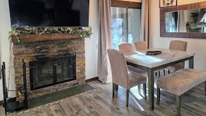 Un área de comedor con chimenea de piedra, un televisor de pantalla plana montado encima y una mesa con sillas.