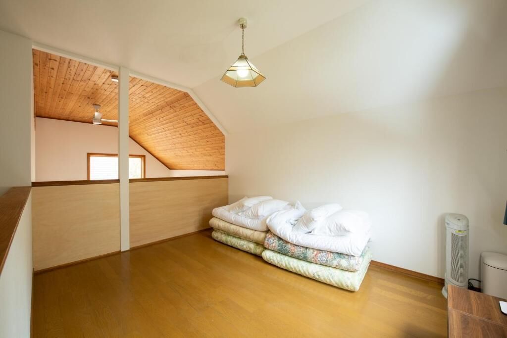 A room with a sloped ceiling, wooden flooring, and a stack of mattresses.