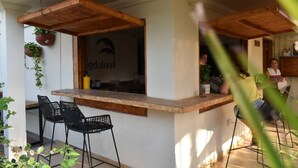 Una zona de bar con un mostrador de madera, dos sillas negras y una planta en maceta.