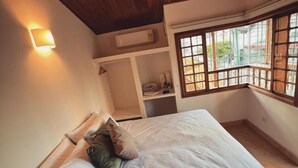 Un dormitorio con techo de madera, una cama con almohadas, una mesita de noche y una ventana con vistas al exterior.