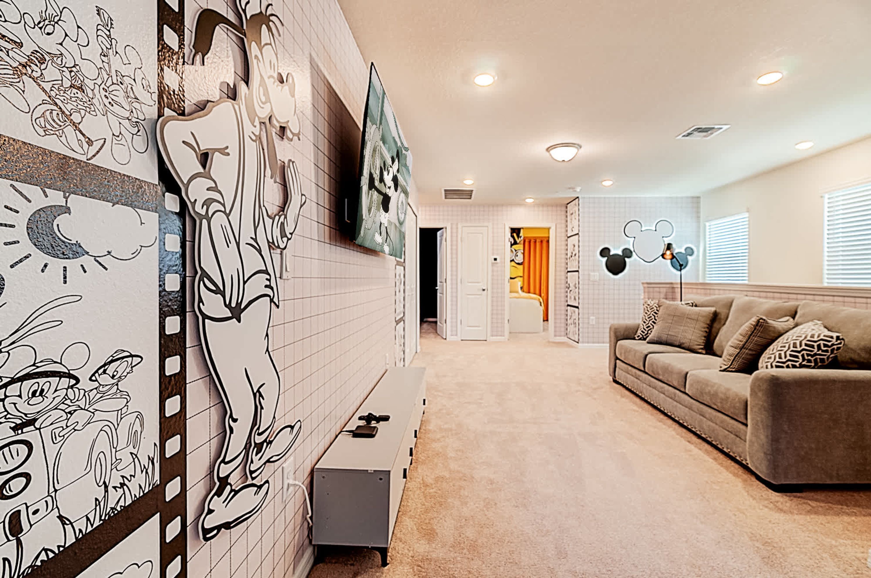 Uma sala de estar com um grande mural na parede, um sofá e um banquinho.