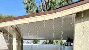 Un patio cubierto con cerca blanca, una silla de mimbre, una planta en maceta y suelo de hormigón.