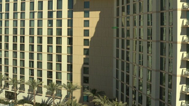 Un hotel moderno de gran altura con una fachada de ventanas enrejadas, balcones y palmeras en primer plano.