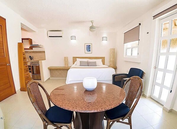A hotel room with a bed, a dining table with chairs, a ceiling fan, and a window.