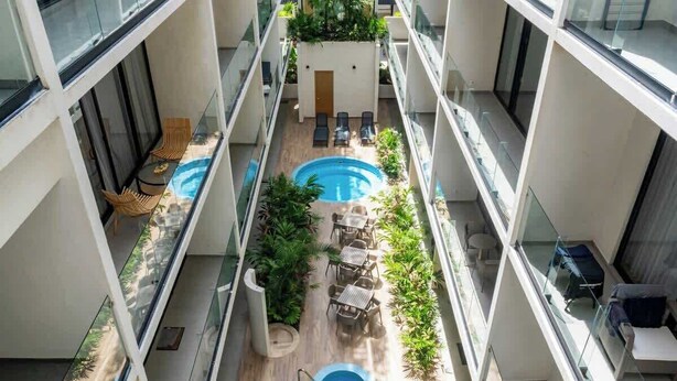 A multi-level indoor pool area with glass railings, lounge chairs, and tables. - Studio w/ Balcony | Pools, Gym, Steps to Beach (Playa del Carmen)