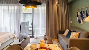 A modern hotel room with a bed, a sofa, a dining table with breakfast items, and a TV. - Studio w/ Balcony | Pools, Gym, Steps to Beach (Playa del Carmen)