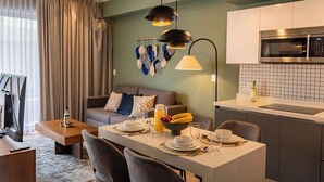 A modern living room with a sofa, dining table, and kitchen area with a microwave. - Studio w/ Balcony | Pools, Gym, Steps to Beach (Playa del Carmen)