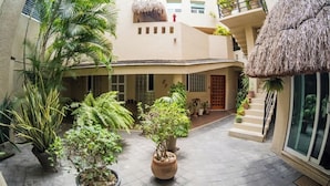 Un patio con plantas en macetas, una estructura con techo de paja y una escalera que lleva a un nivel superior.